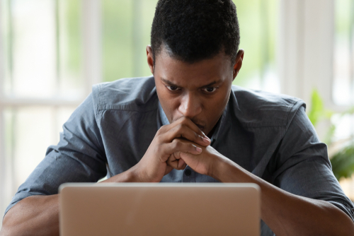An African-American man staring at his computer, upset