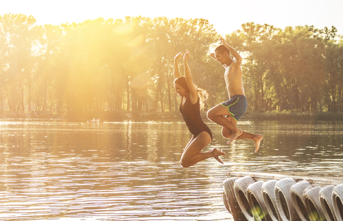 young man and woman jumping off dock into pond