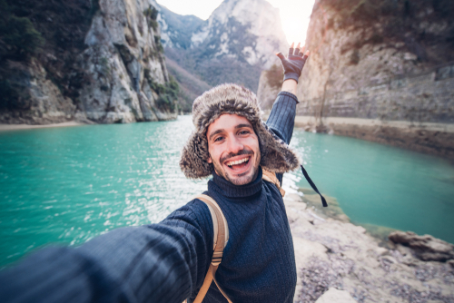  Happy traveller man takes a selfie photo on a lake at the mountain