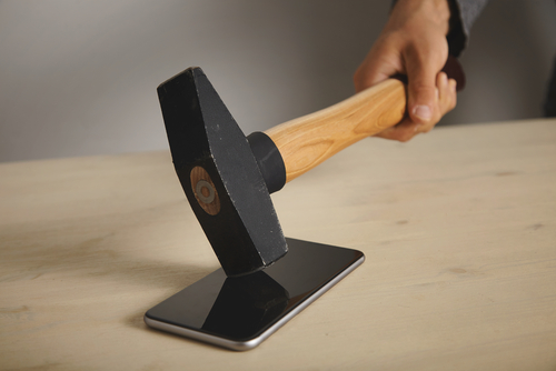 A man is breaking a smartphone lying on a wooden table with a big hammer