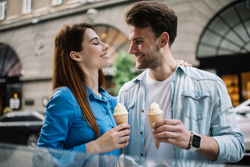  woman in blue shirt and pleased man in casual clothes hugging and enjoying each other while holding ice cream cones 