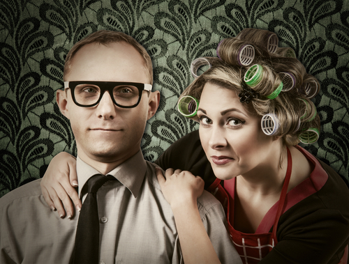 woman in curlers and house dress next to man in thick glasses and tie