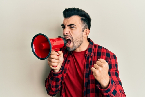 man with stubble and flannel shirt yelling into megaphone