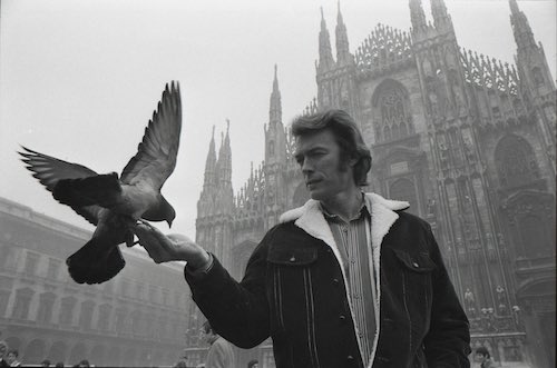 black and white photo of Clint Eastwood holding out his hand and feeding a pigeon in Milan, Italy 1971