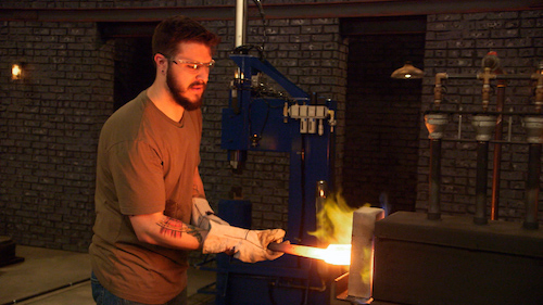 Forged in Fire contestant drawing their glowing-hot billet from the forge