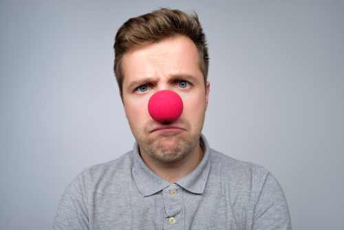 Mature caucasian man wearing clown red nose isolated on gray background