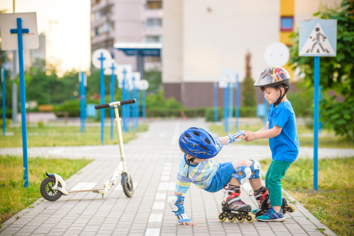 Two boys sibling brothers together in park, helps boy with roller skates to stand up after fall
