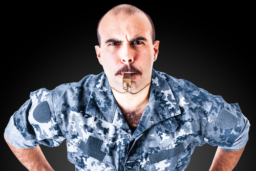 caucasian drill sergeant in blue camo fatigues blowing a whistle over a dark backdrop