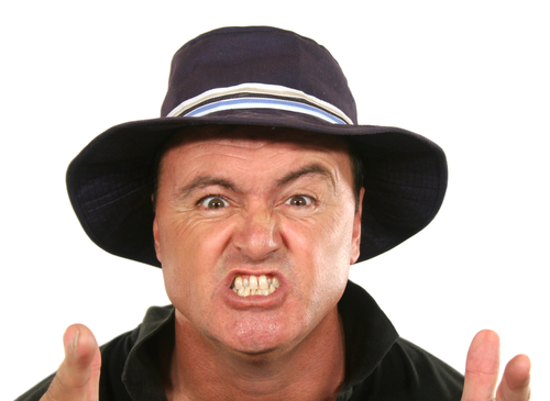 Angry middle aged man in a blue hat pointing index fingers at camera