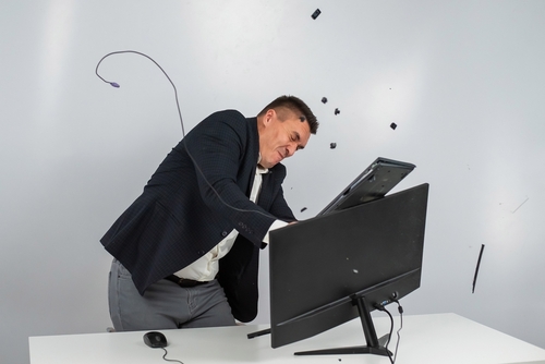 Caucasian man in a suit gets angry and smashes the keyboard on the monitor.