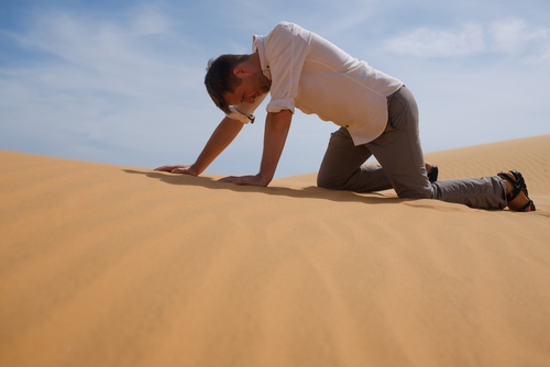 Man in office clothes crawling on hands and knees in the sunny desert.