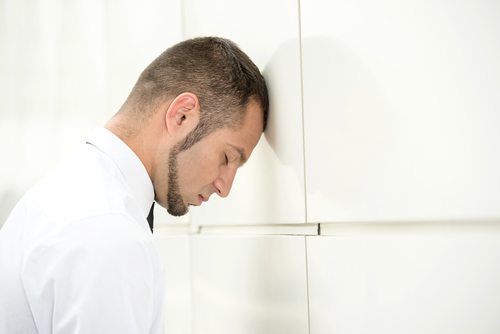 White man in white oxford shirt, resting head against wall