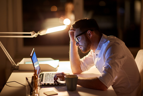 hombre de negocios estresado en gafas con computadora portátil escribiendo en la oficina nocturna