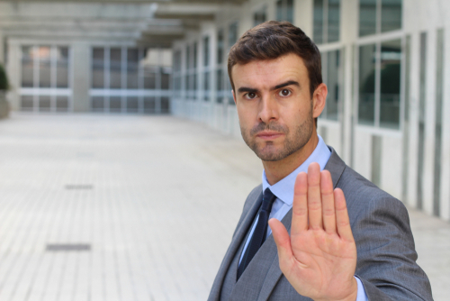 Businessman in a gray suit scowling and holding up a hand to say "stop"