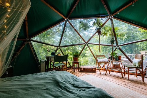 inside a dome tent in a forest, with chairs, a desk and a large comfortable bed