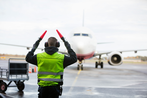 Personal de tierra con chaleco de alta visibilidad, de espaldas a la cámara, señalando al avión en la pista mojada