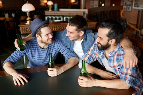 happy male friends drinking bottled beer and hugging at bar