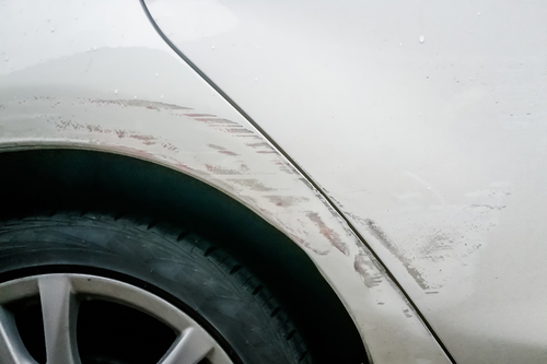The side of white car, with scratches around the wheel well and door