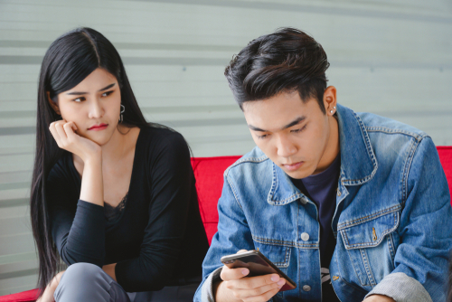 Mujer asiática atractiva molesta mirando a su novio usando un teléfono inteligente.