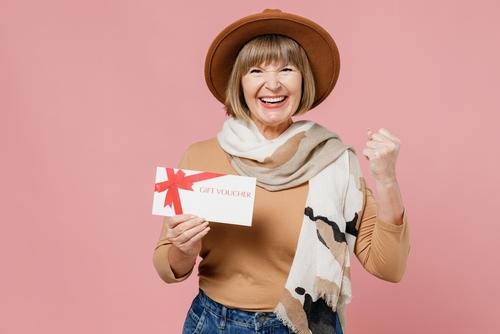 elderly senior woman 55 years old wears brown shirt hat scarf holding a gift certificate 